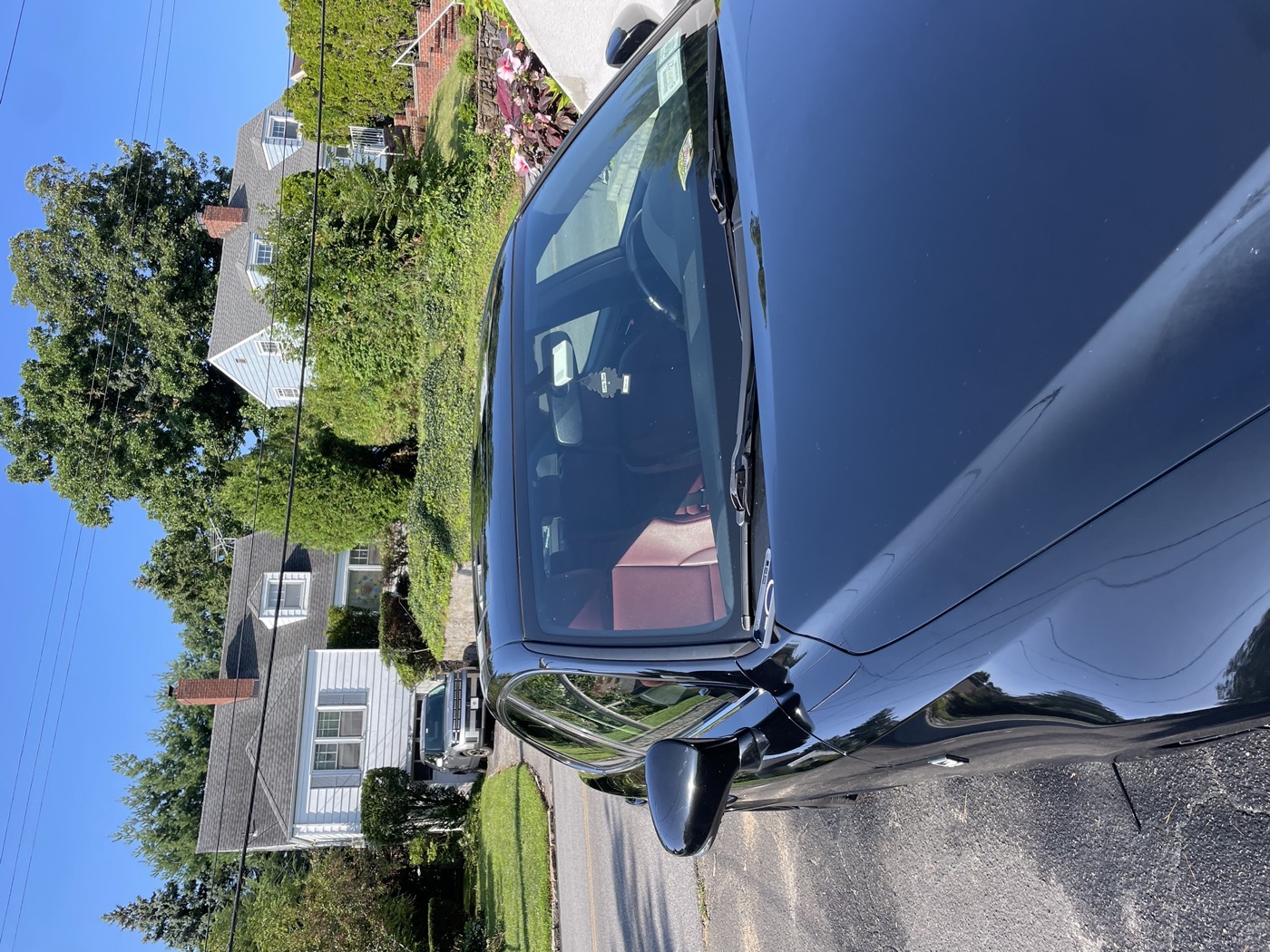 Glossy black sedan hood and windshield after full detail, reflecting the sky and surrounding houses